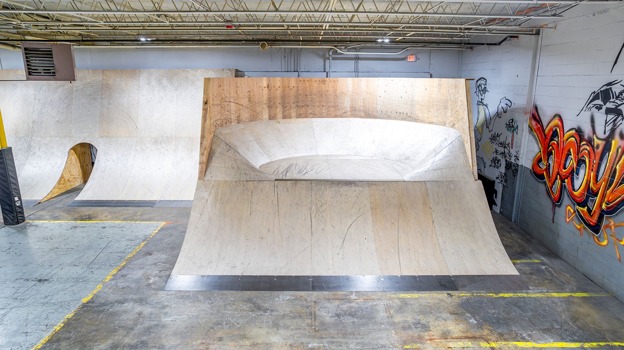 Wooden BMX ramp inside a warehouse with graffiti on the walls.
