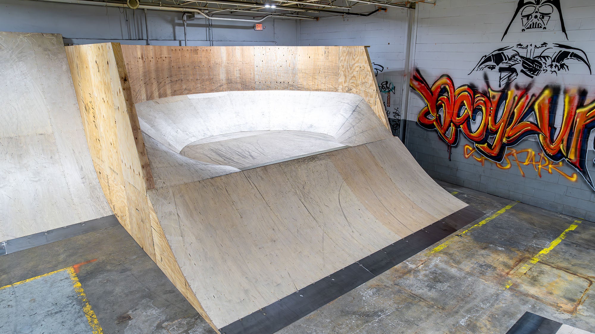 Wooden BMX ramp inside a indoor skate park with graffiti on the wall.