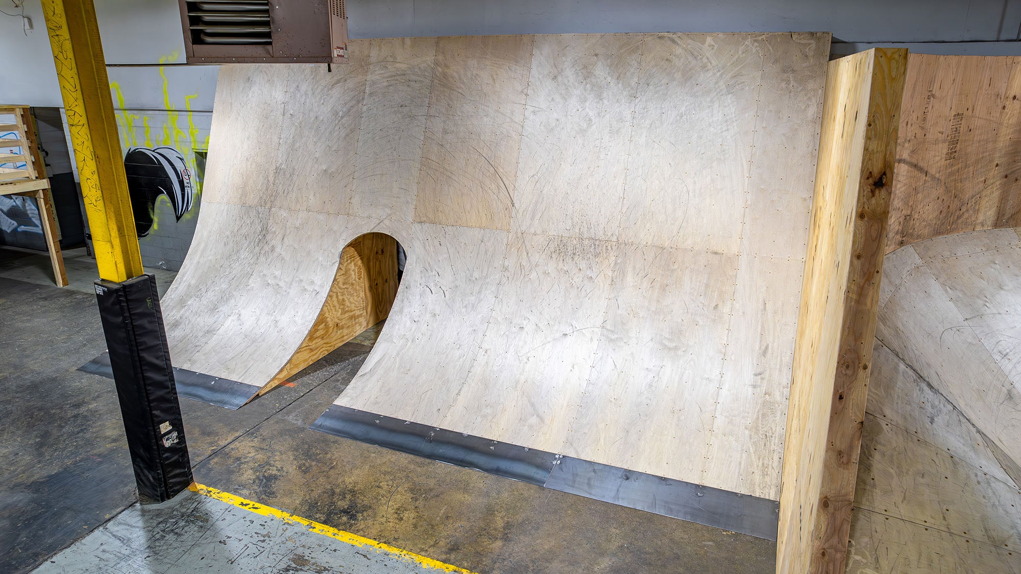 Wooden BMX ramp inside a building with a concrete floor.