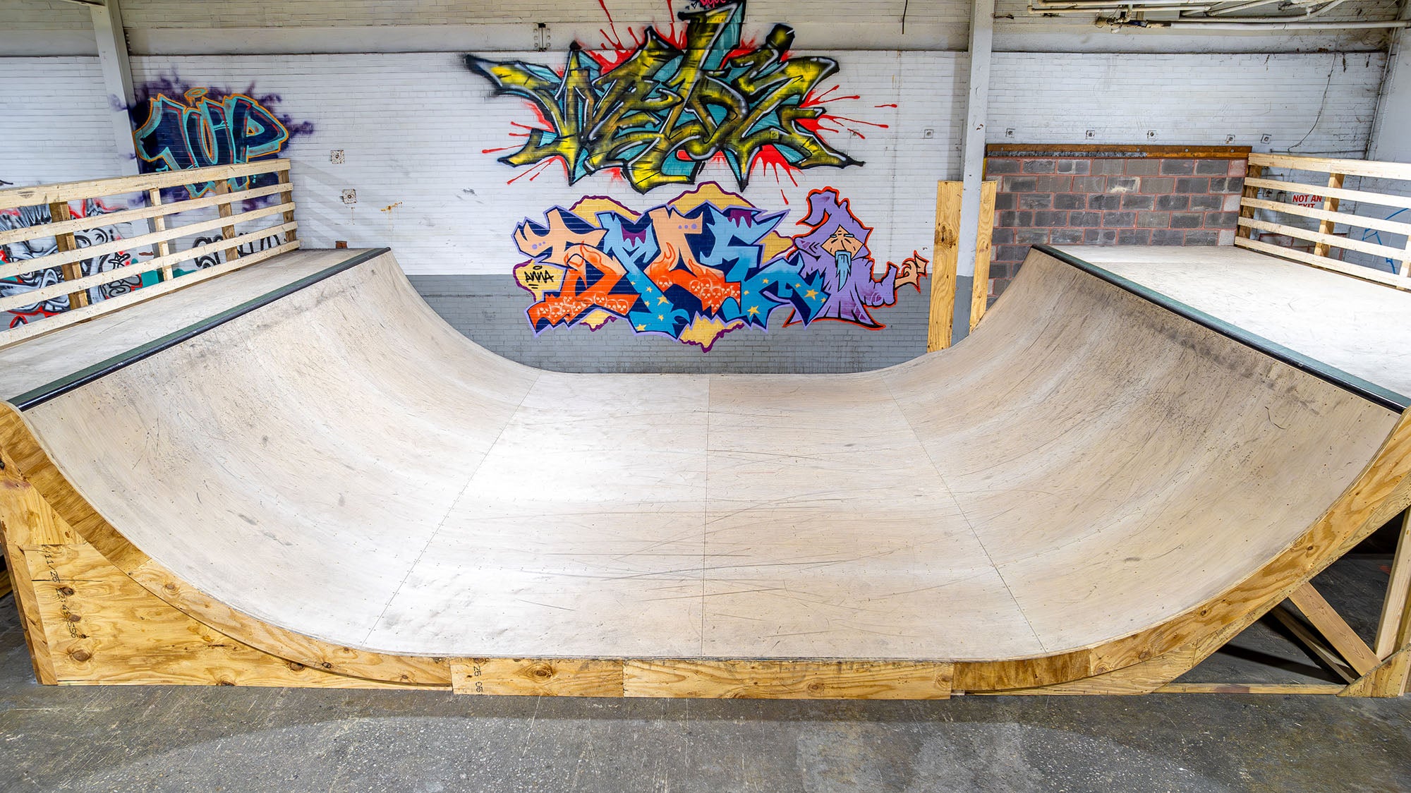 Wooden BMX mini ramp with colorful graffiti art on a wall inside a skate park.