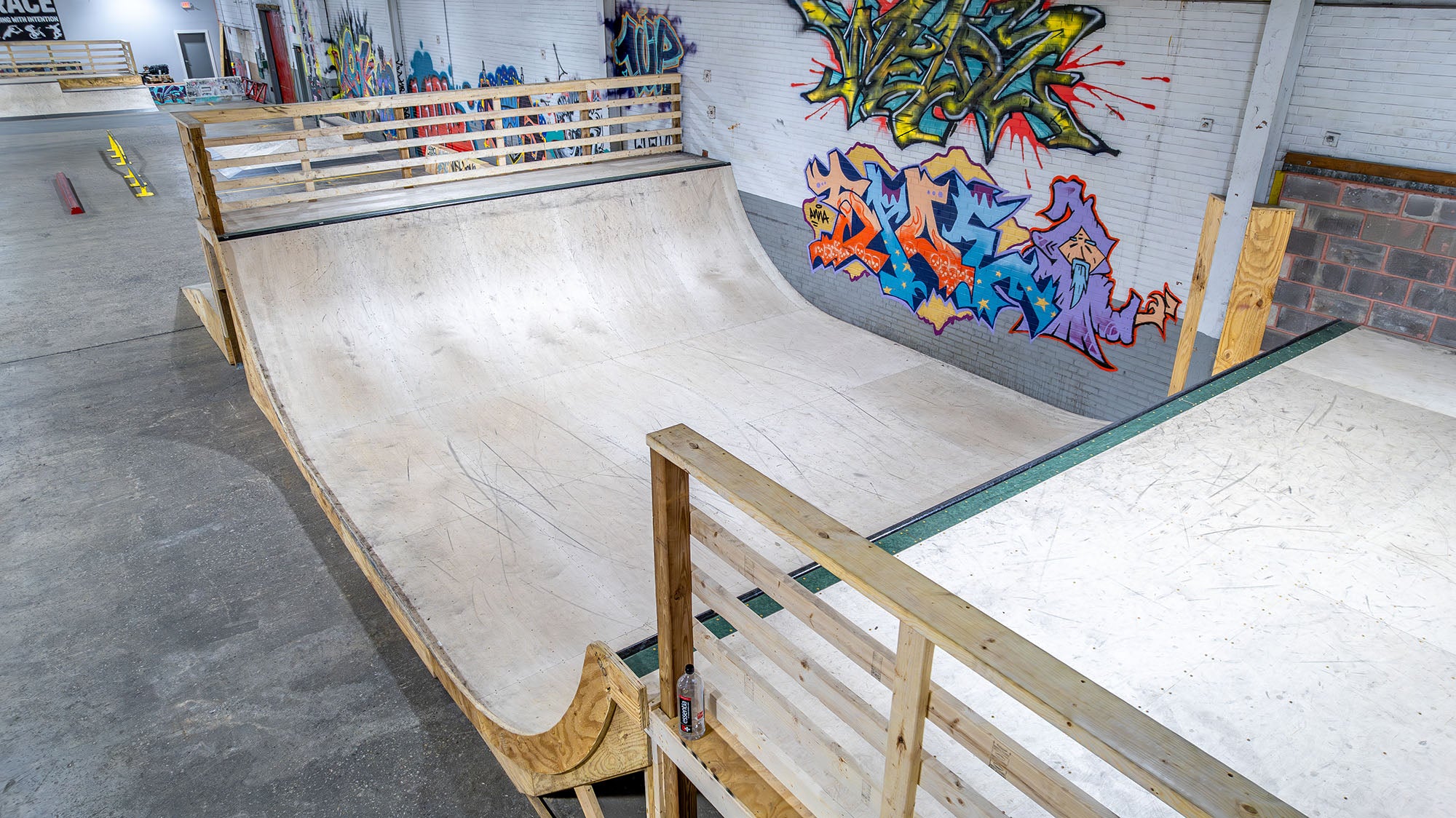 Indoor skate park with wooden ramps and colorful graffiti on the wall.