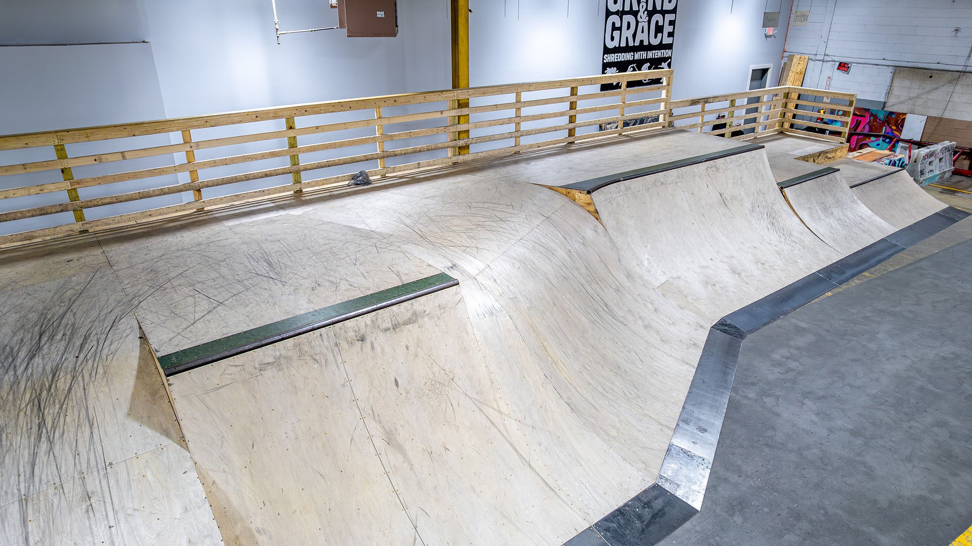 Indoor skate park with wooden ramps and a railing.