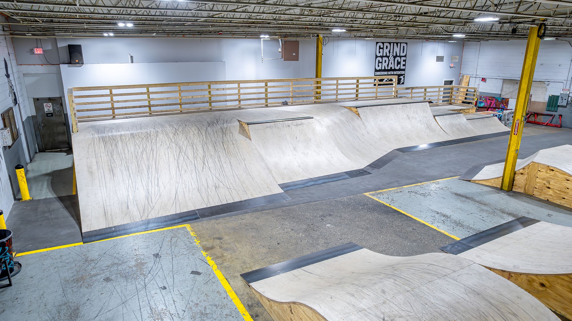 Indoor skate park with various ramps and a 'Grind & Grace' sign on the wall.