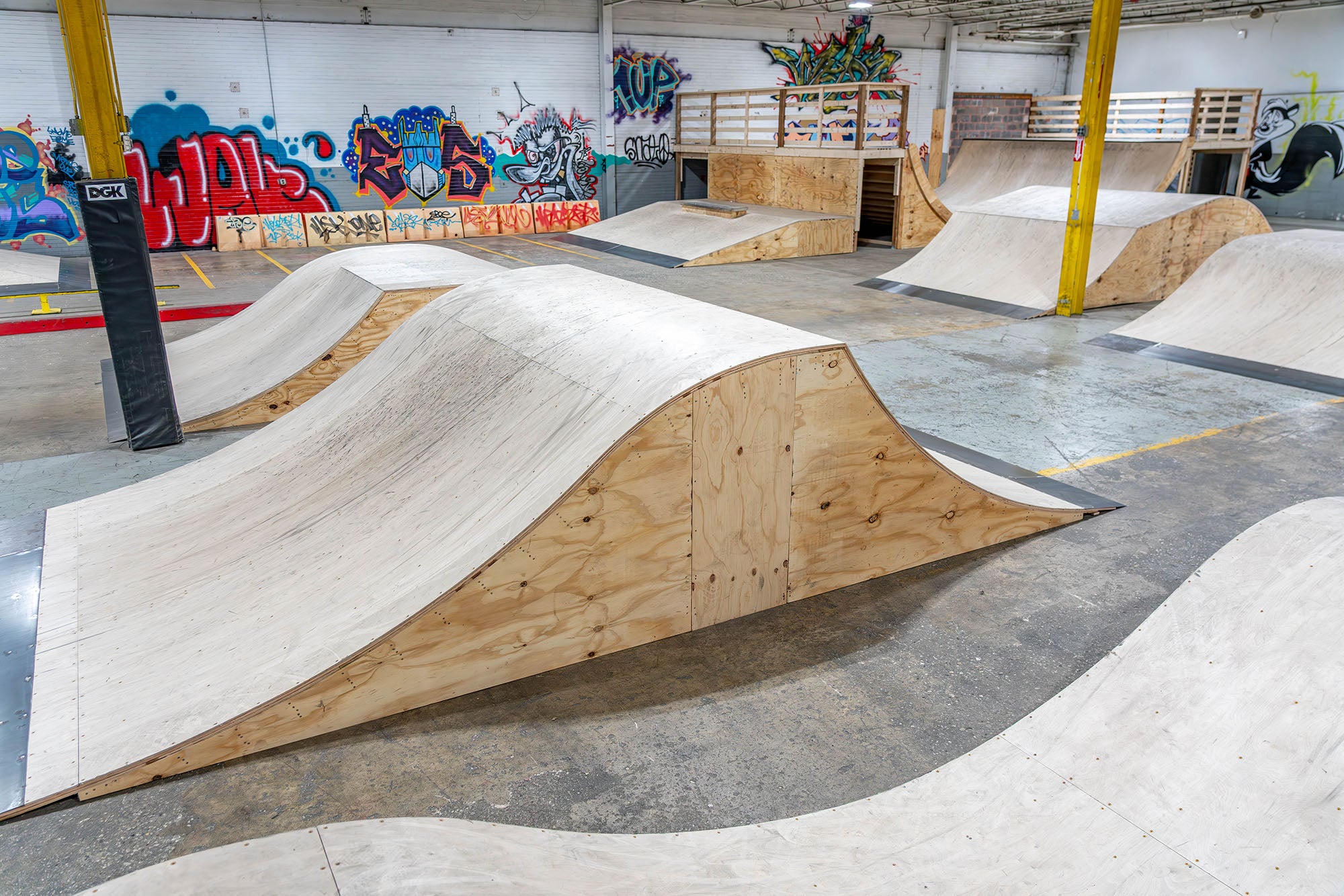 Wooden ramps and BMX park with graffiti on the walls in an indoor skate park.