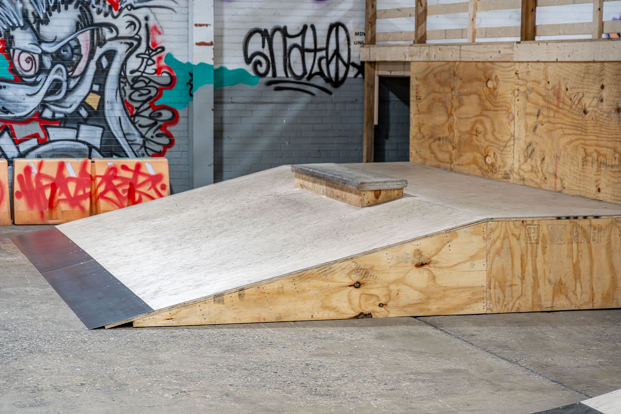 Wooden ramp with a grind-able ledge in an urban setting with graffiti on the wall.