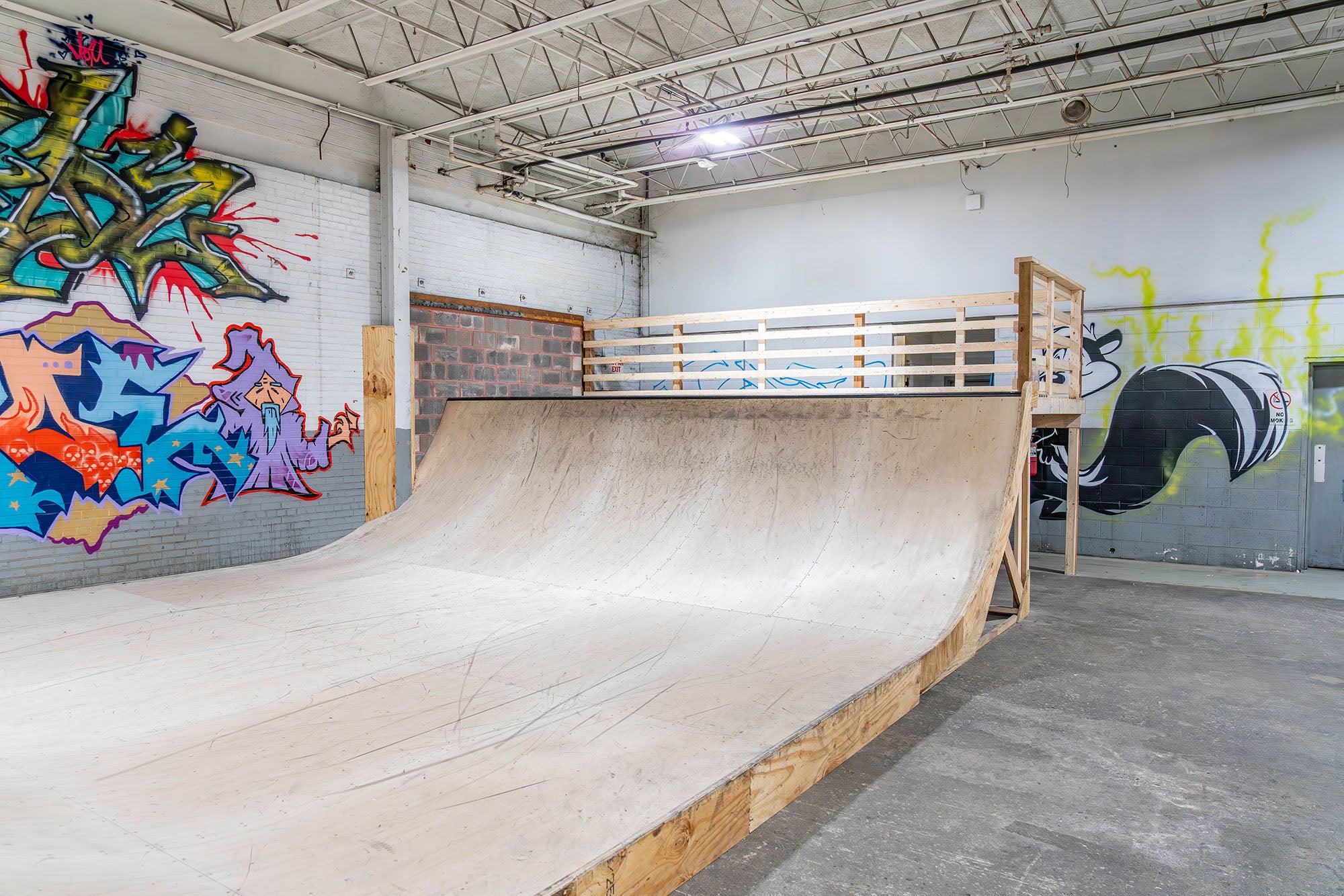 Indoor skate park with a wooden ramp and colorful graffiti on the walls.