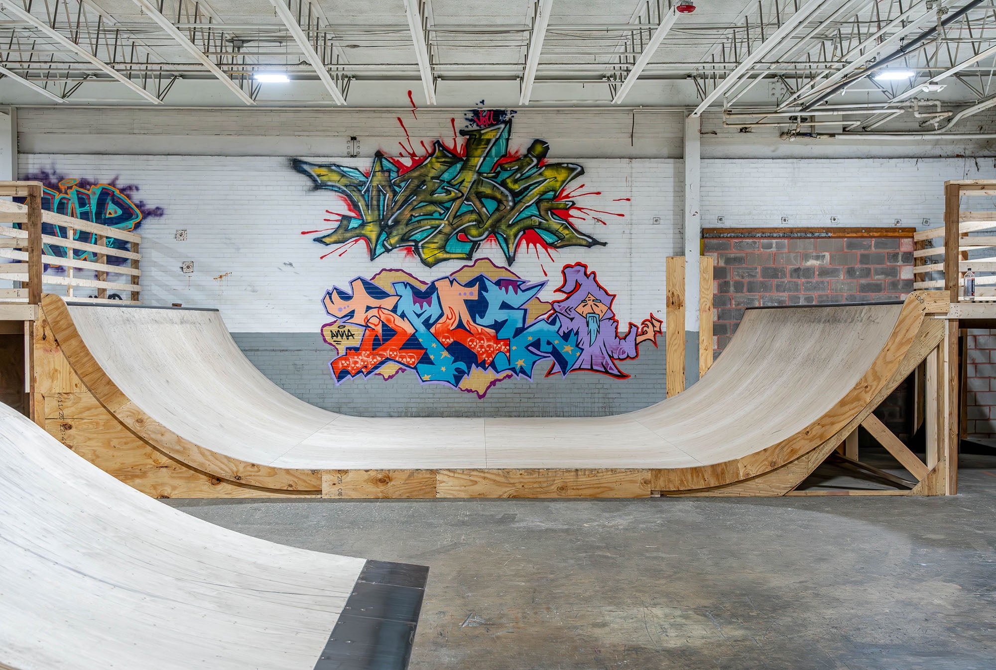 Indoor skate park with wooden mini-ramp and colorful graffiti art on the wall.