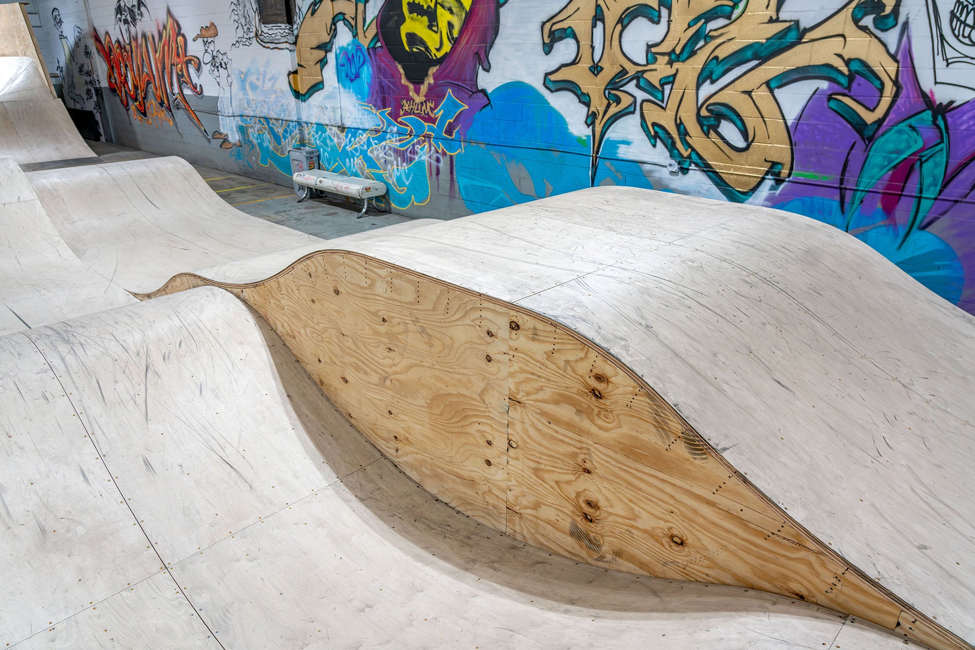 Wooden BMX ramp in a skate park with colorful graffiti on the wall.
