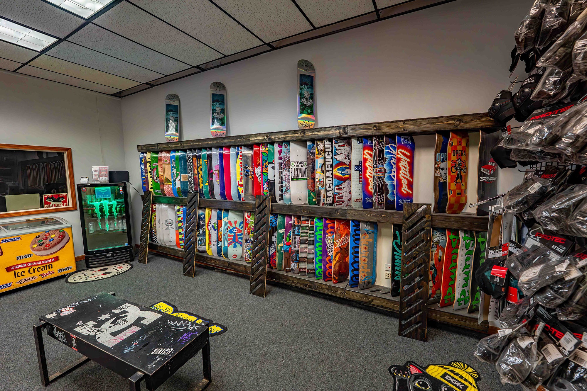 Room with skateboard decks on wooden racks and a table with a skateboard design.