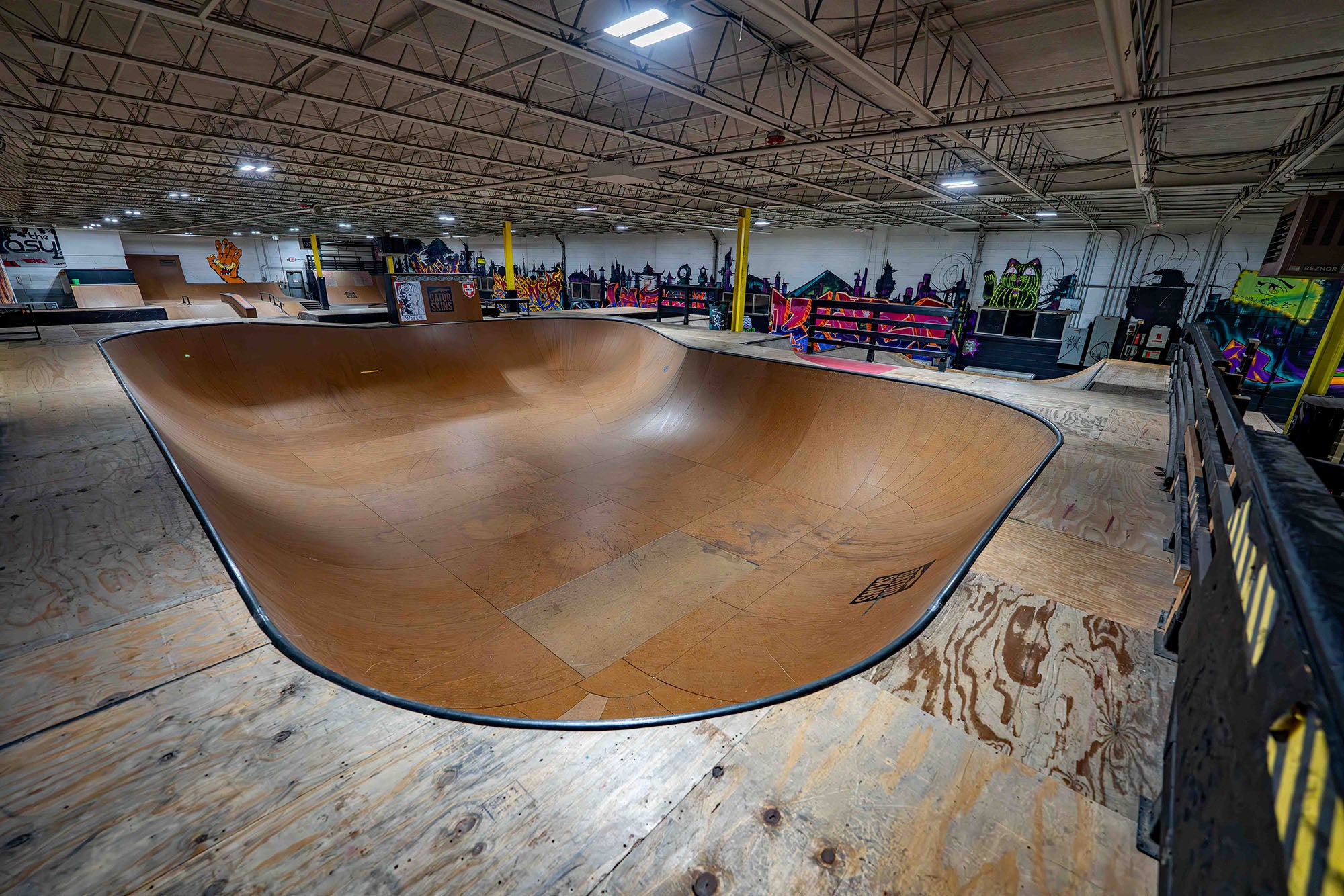 Indoor skate park with a large wooden bowl and various skateboarding equipment.