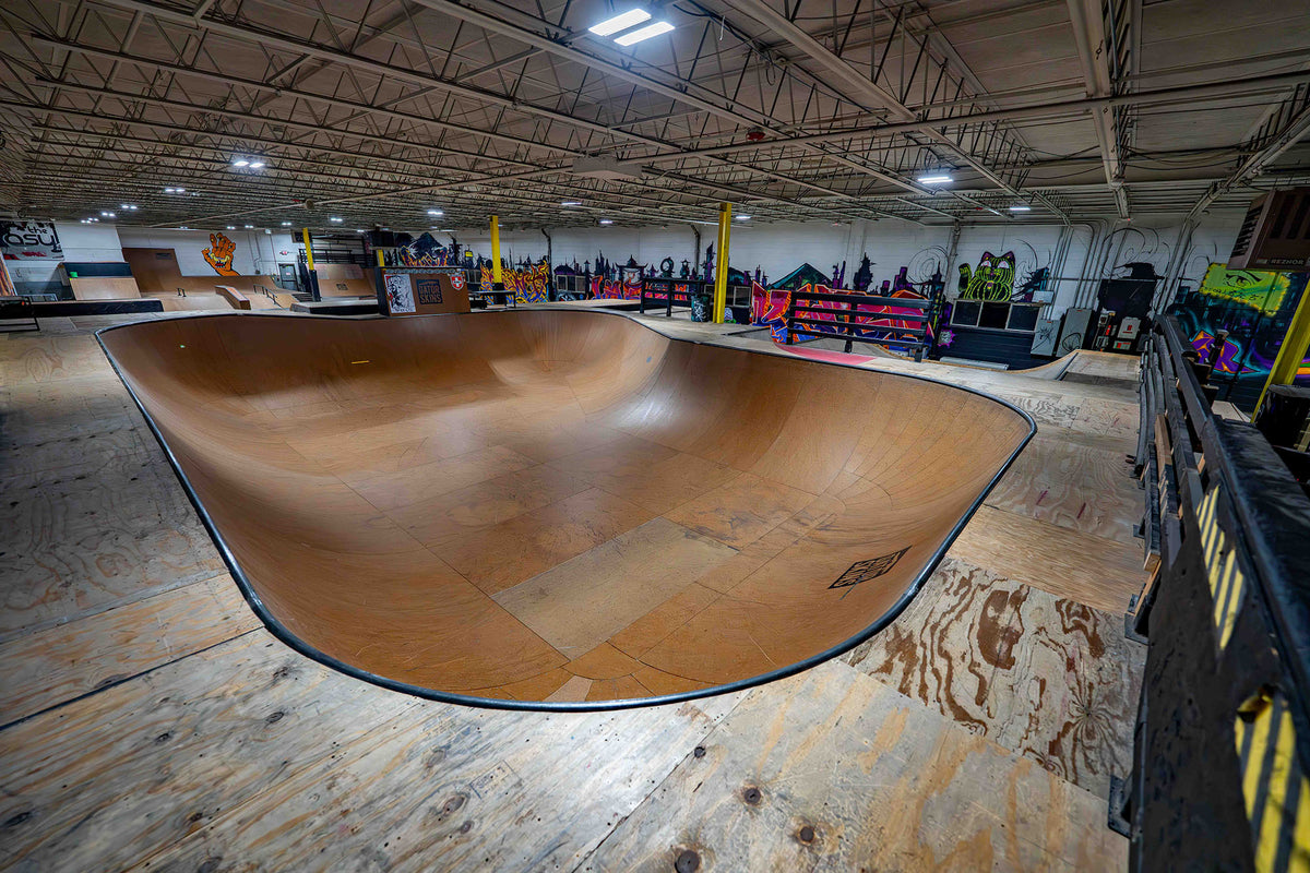 Indoor skate park with a large wooden bowl and various skateboarding equipment.