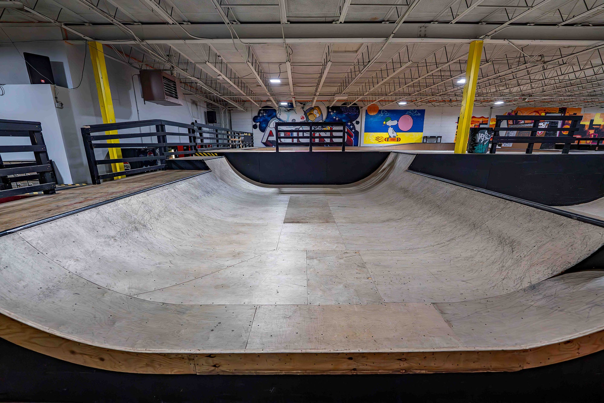 Skateboard ramp inside a indoor skate park with various equipment and posters on the wall.