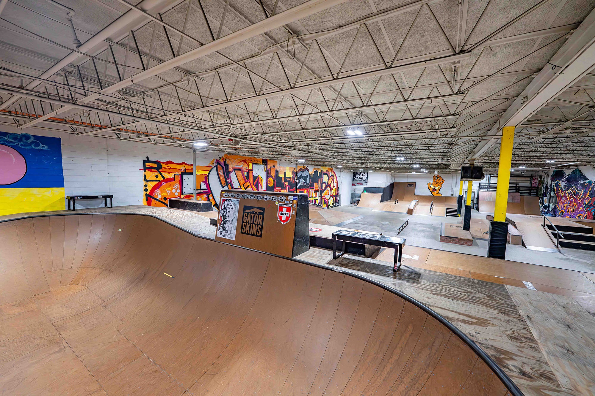 Indoor skate park with wooden ramps and colorful murals on the walls.
