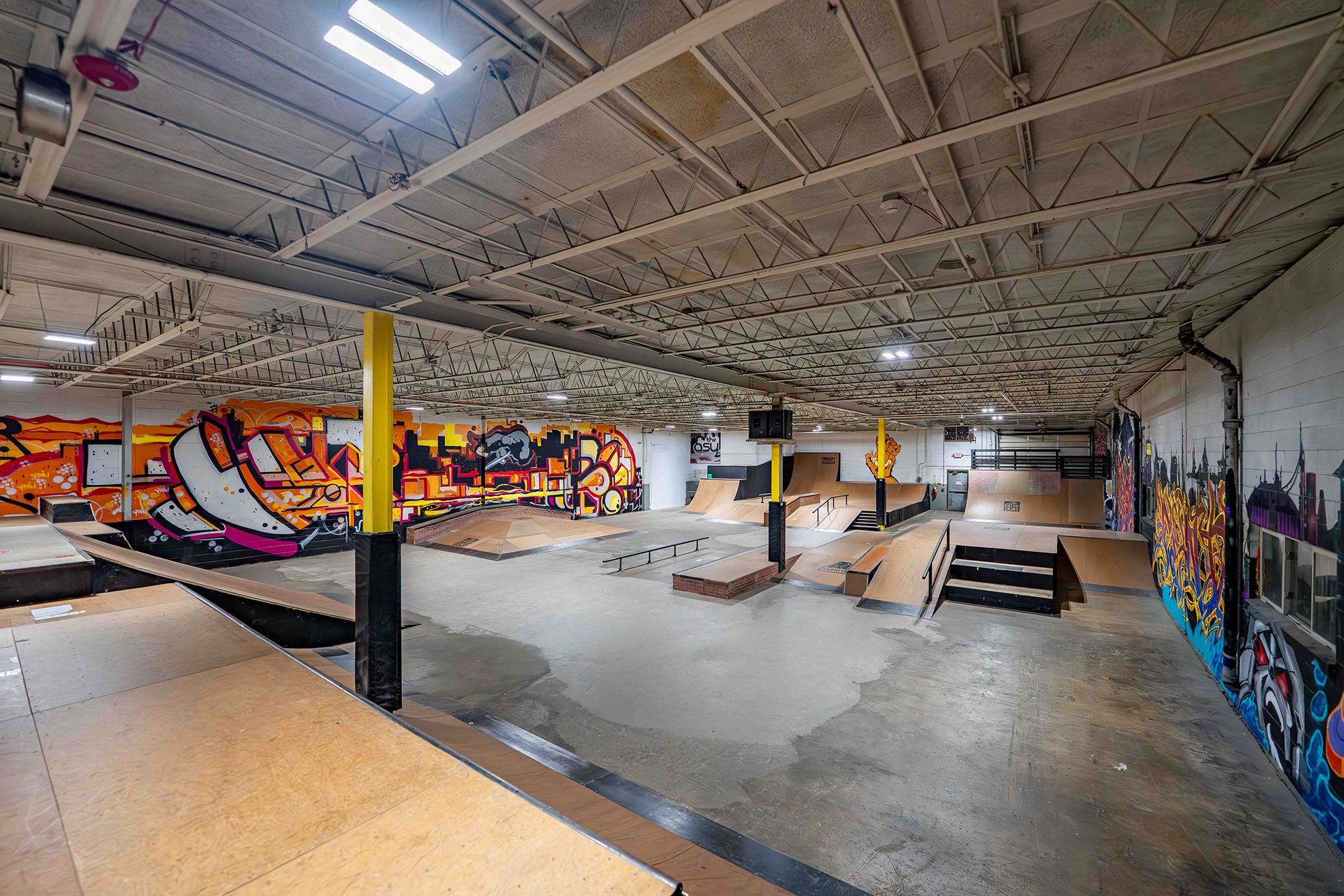 Indoor skate park with various ramps and graffiti art on the walls.