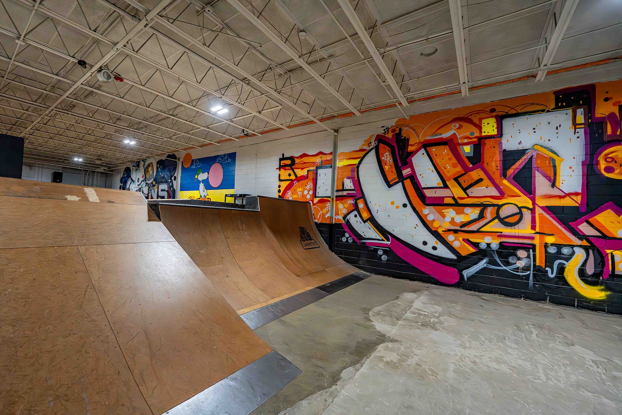 Skate park with wooden ramps and colorful graffiti art on the wall.