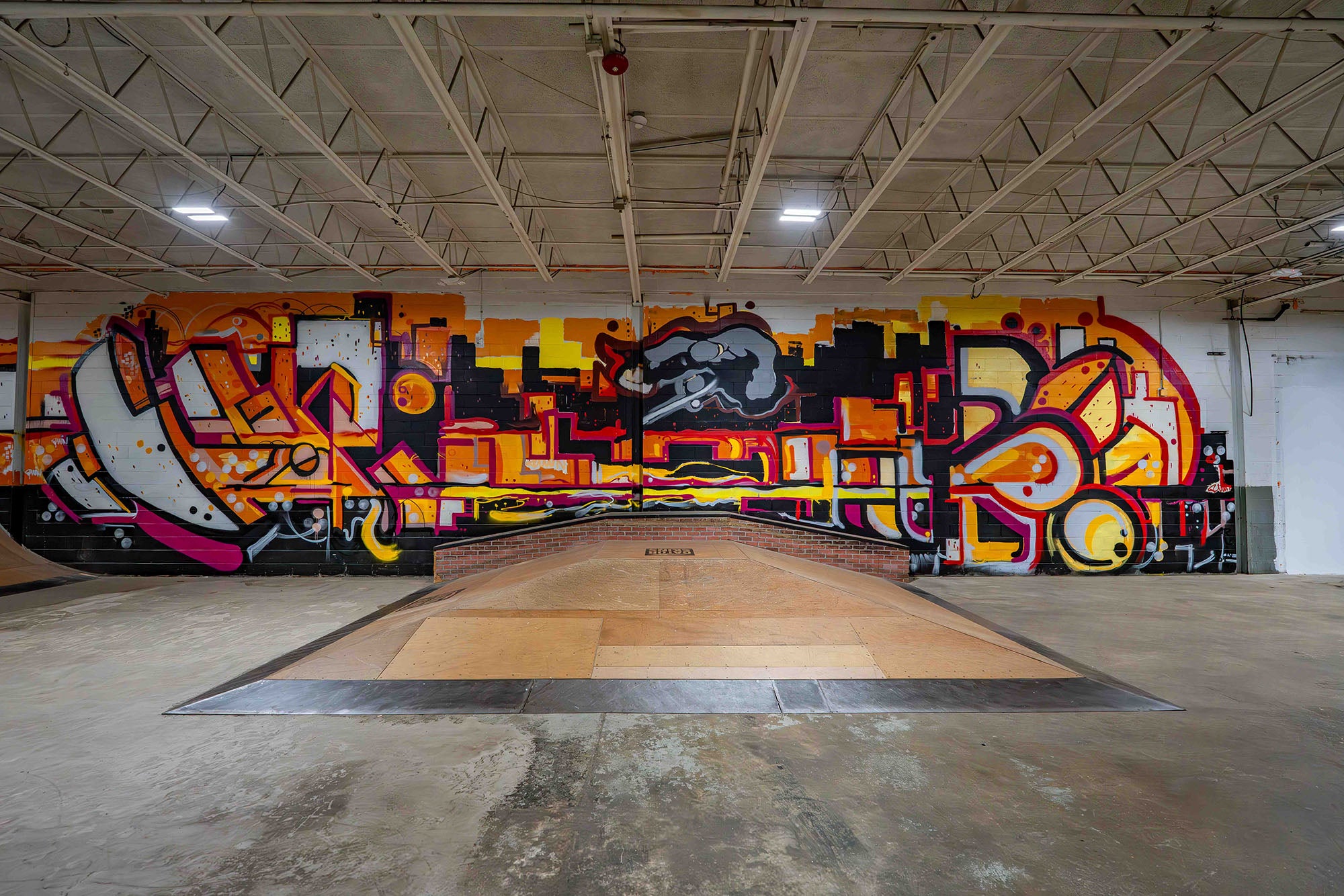 Graffiti art on a wall in an indoor setting with concrete floor and high ceiling.