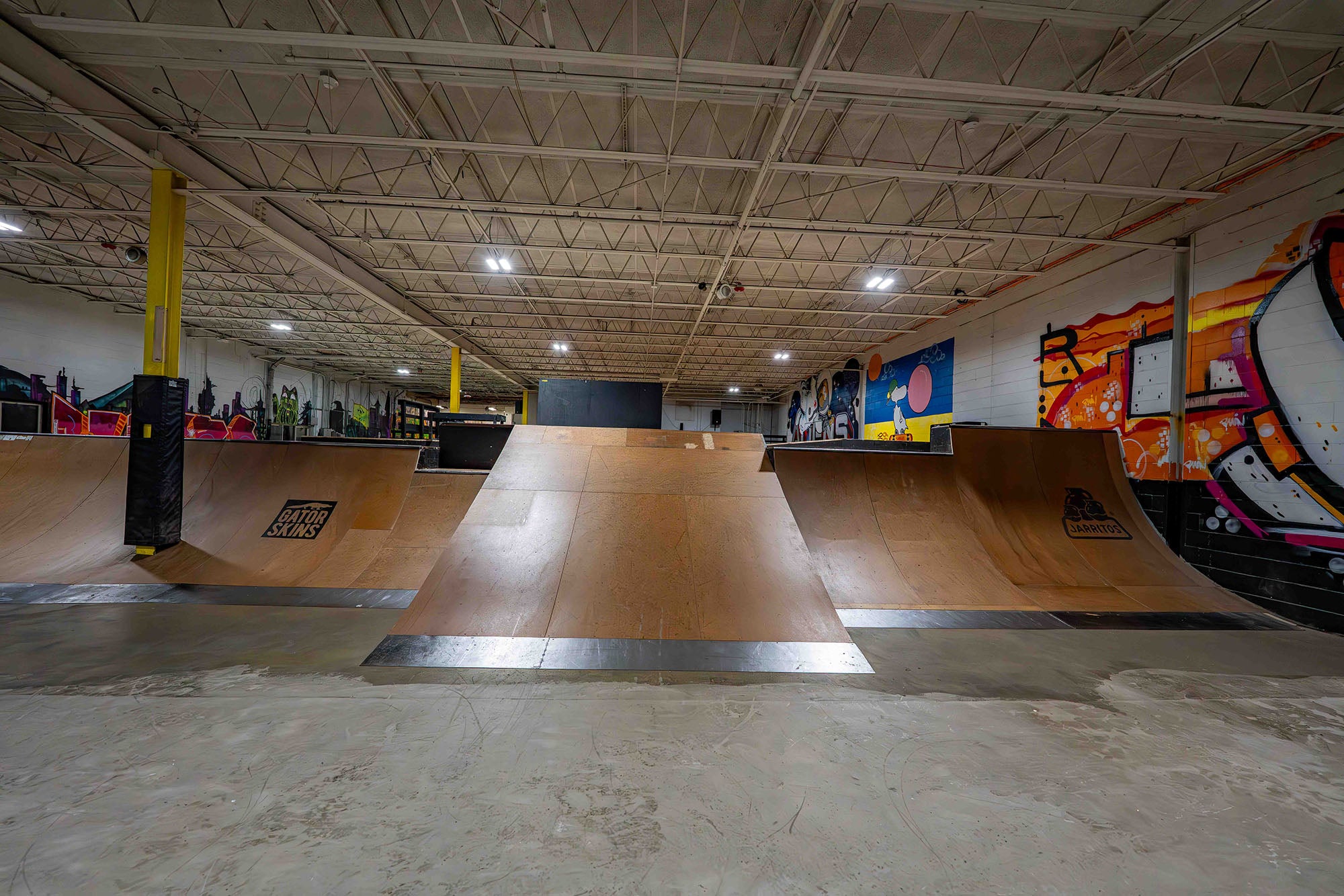 Indoor skate park with wooden ramps and colorful wall art.