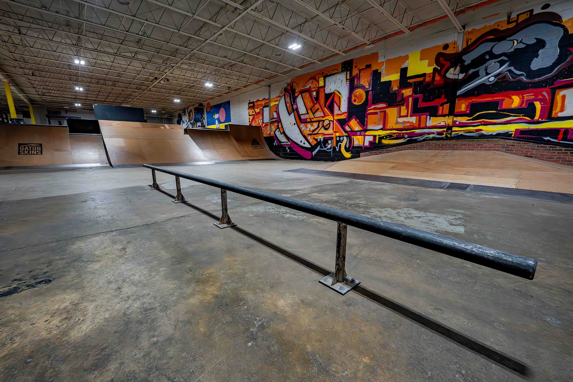 Skate park with a long metal rail and colorful mural on the wall.