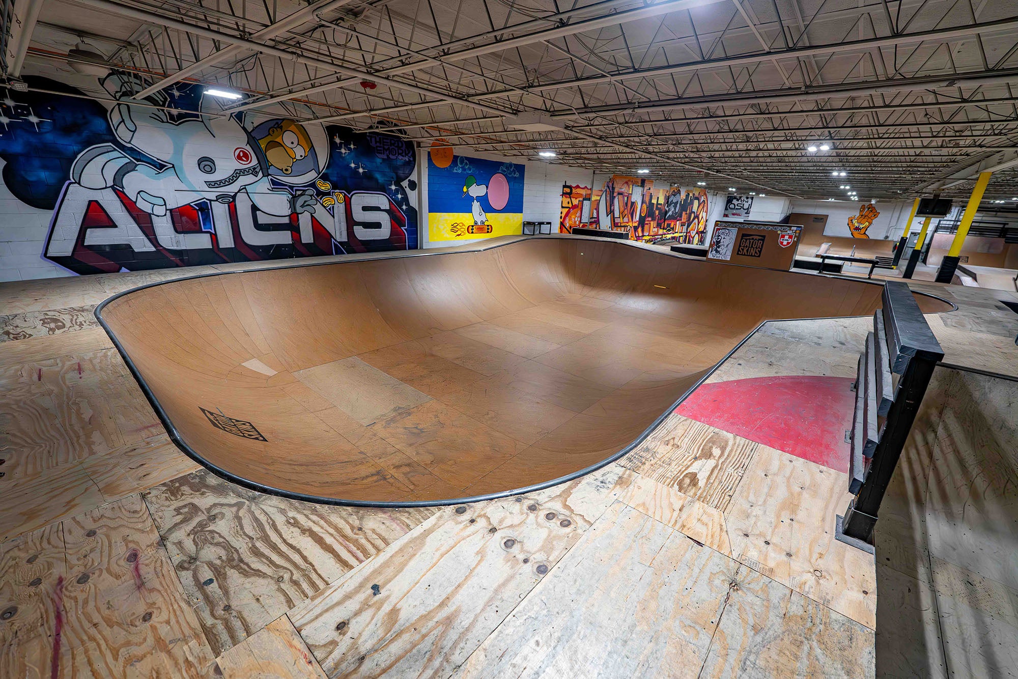 Large indoor skatepark with a wooden bowl and colorful wall art.