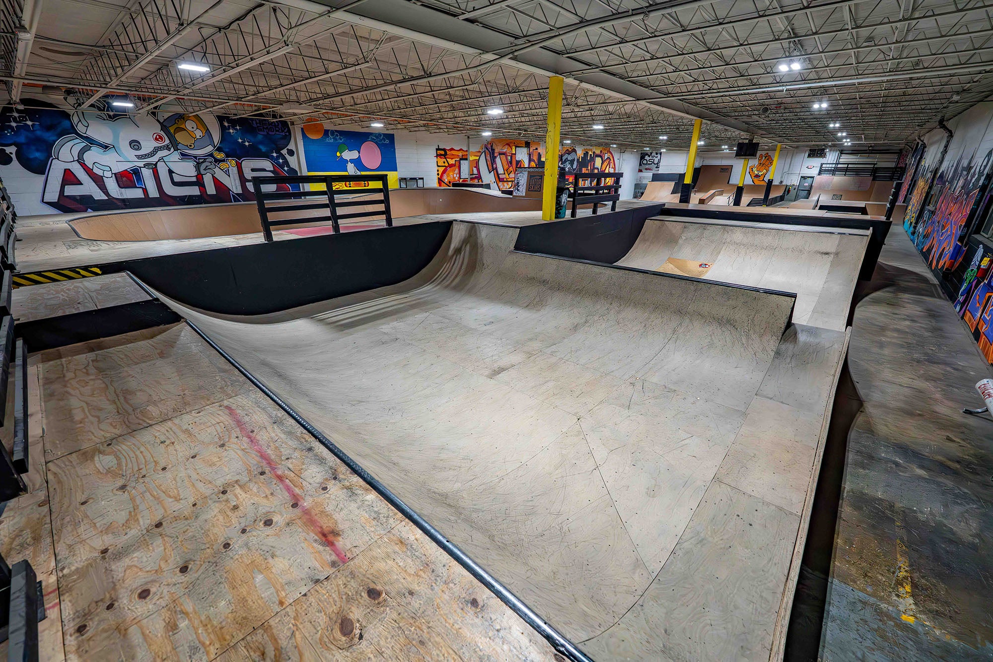 Indoor skate park with various ramps and graffiti art on the walls.